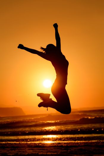 Successful woman jumping, dancing and having fun on sunset in beach. Freedom and happiness concept. Girl celebrating work out success.