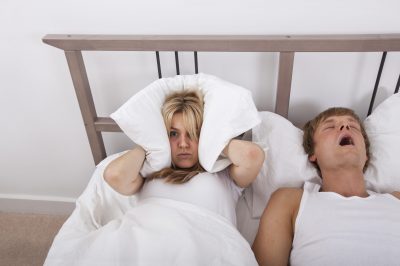Frustrated woman covering ears with pillow while man snoring in bed Frustrated woman covering ears with pillow while man snoring in bed